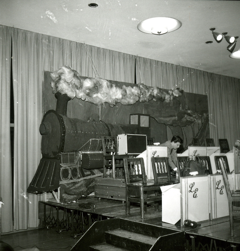 A man prepares the stage for the Les Elgart band with a backdrop of a train for the Homecoming Dance, 1965.