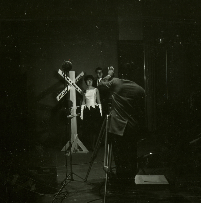 A couple poses by the train crossing sign for a photographer at the Homecoming Dance with the theme Night Train, 1965.