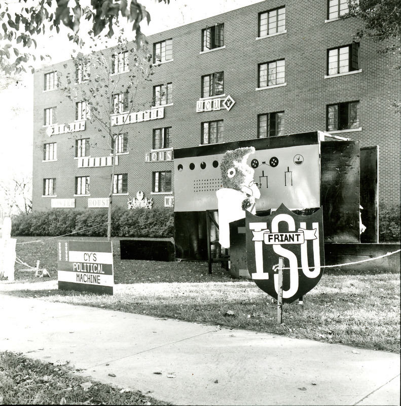 In the Friant House Homecoming lawn display, a bespectacled Cy in a white lab coat operates a large box-like device labeled Cy's Political Machine, 1968.