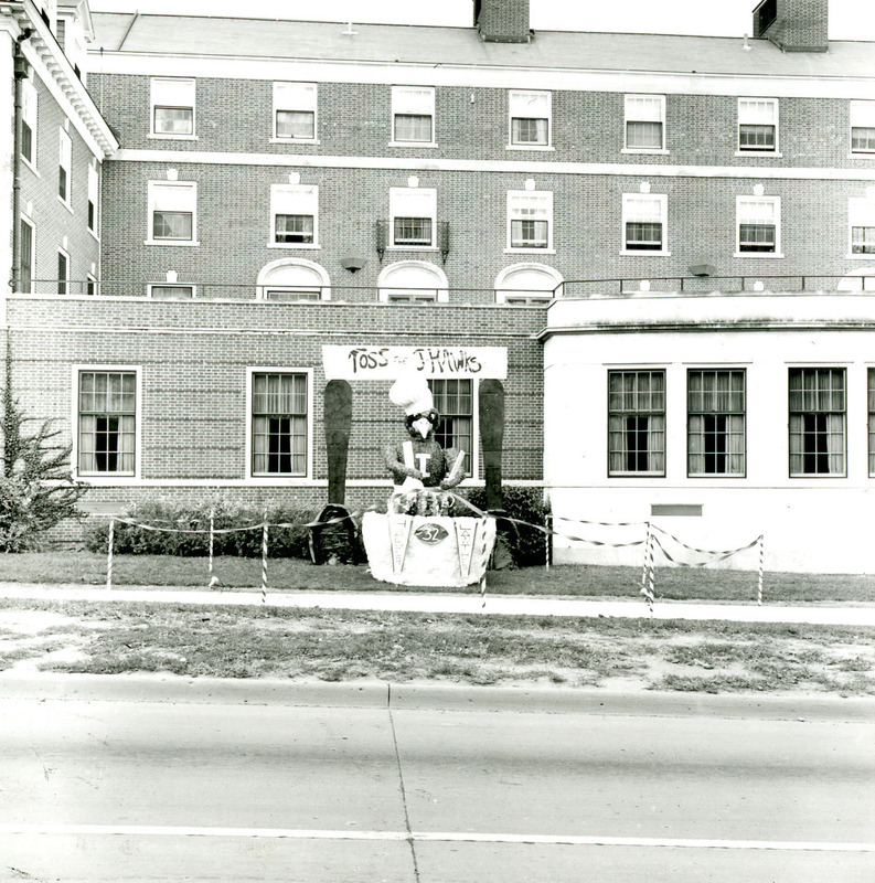 The Haber House and Lawther House Homecoming lawn display shows Cy wearing a chef's hat and tossing a salad to Toss the J-Hawks, outside the Linden Hall cafeteria, 1968.