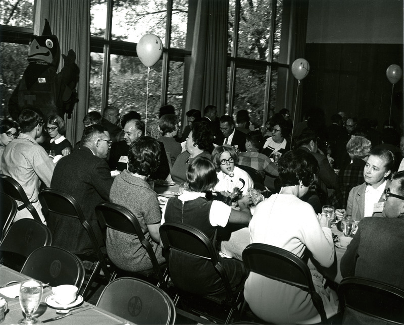 Alumni sit at tables in the Memorial Union for the Homecoming Banquet while Cy waves in the background, 1969.