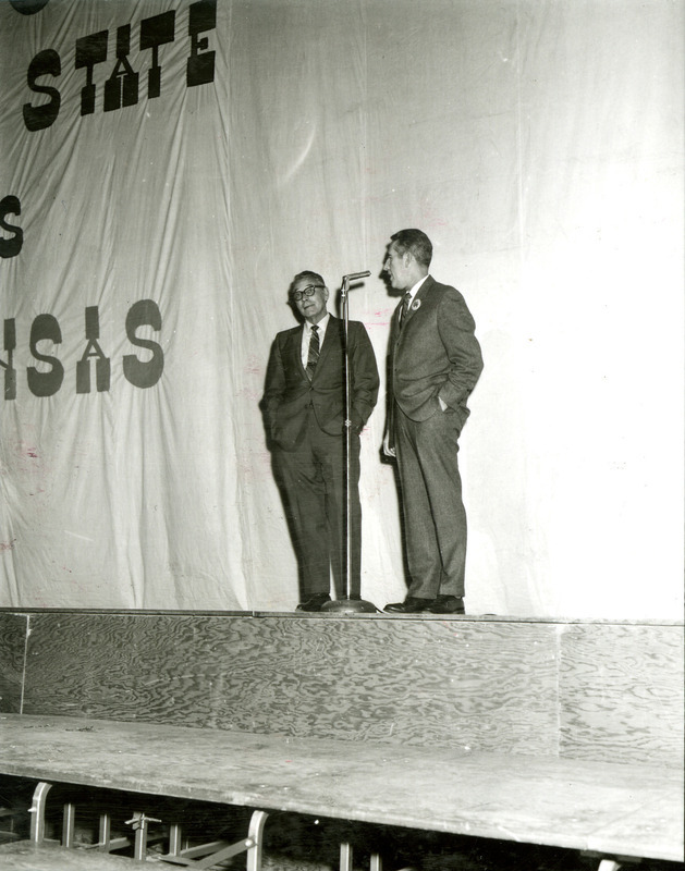 President Parks speaking at the microphone on stage with another man on stage on the night before Homecoming, 1969.