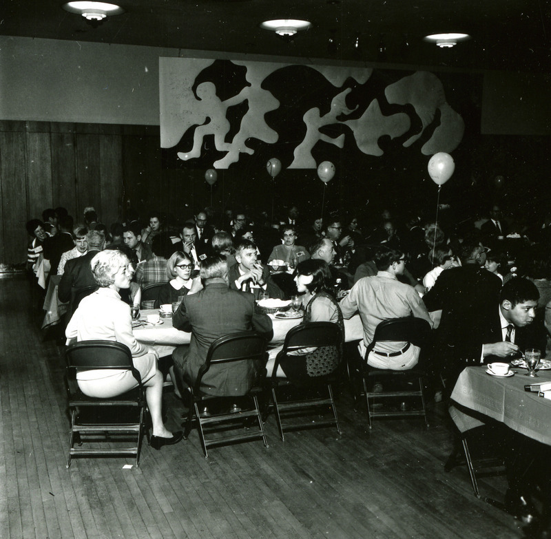 Alumni sit at tables for the Homecoming Banquet with a modern work of art in the background, 1969.