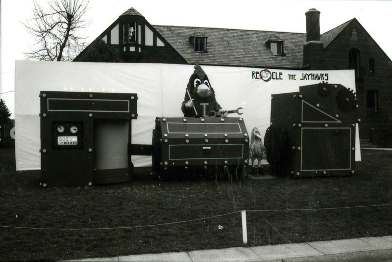 Homecoming lawn display by Sigma Phi Epsilon, Iowa Beta chapter, shows Cy operating equipment to "ReCYcle the Jayhawks," 1977.