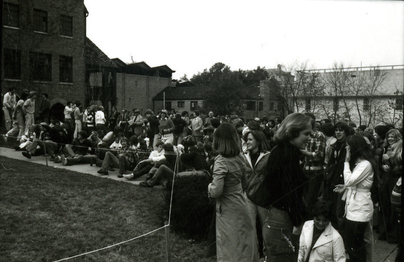 A crowd gathers next to a roped-off area among the Greek houses to wait for announcements of the lawn display winners for Homecoming, 1977.