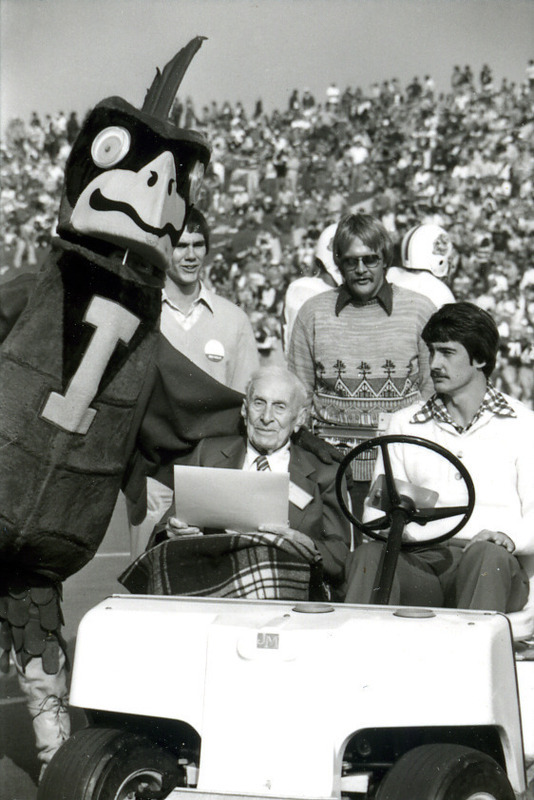 Cy hugs 100-year-old alumnus, Mr. Kelly, who is being driven on the football field during Homecoming, 1977.