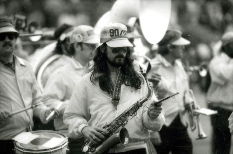 A long-haired saxophone player and a drummer are shown marching in the ISU Alumni Band at Homecoming, 1985.