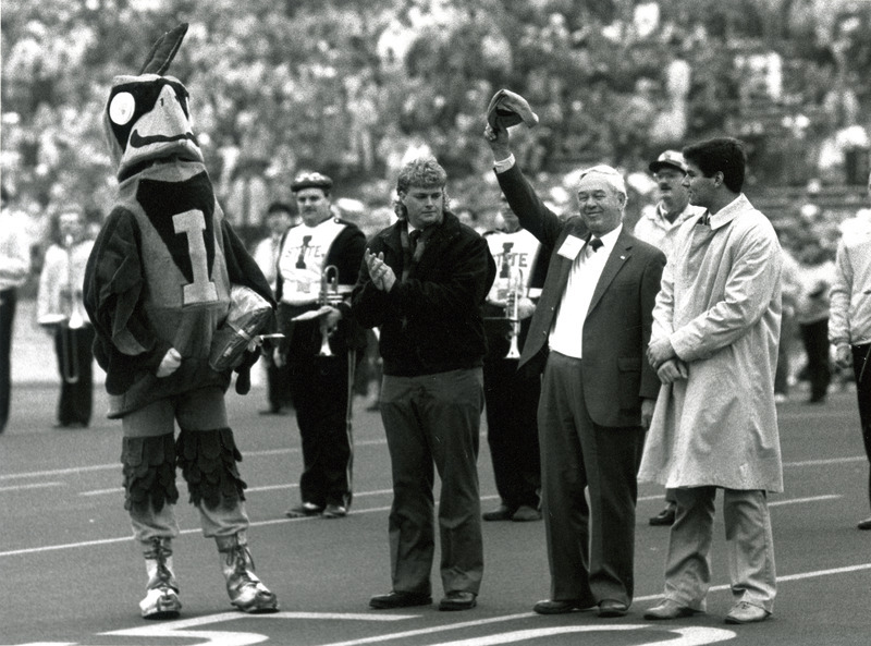 Bob Eddy, named Cy's Favorite Alum, raises his cap at Homecoming Game halftime, 1987. He is flanked by (left to right) Cy and General Co-Chairs Marty Epy and Terry Helphrey.