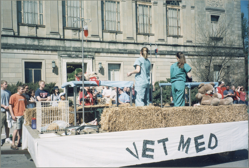 A VEISHEA parade float from the College of Veterinary Medicine. Two female students in scrubs are on the float along with stuffed animals on exam tables.