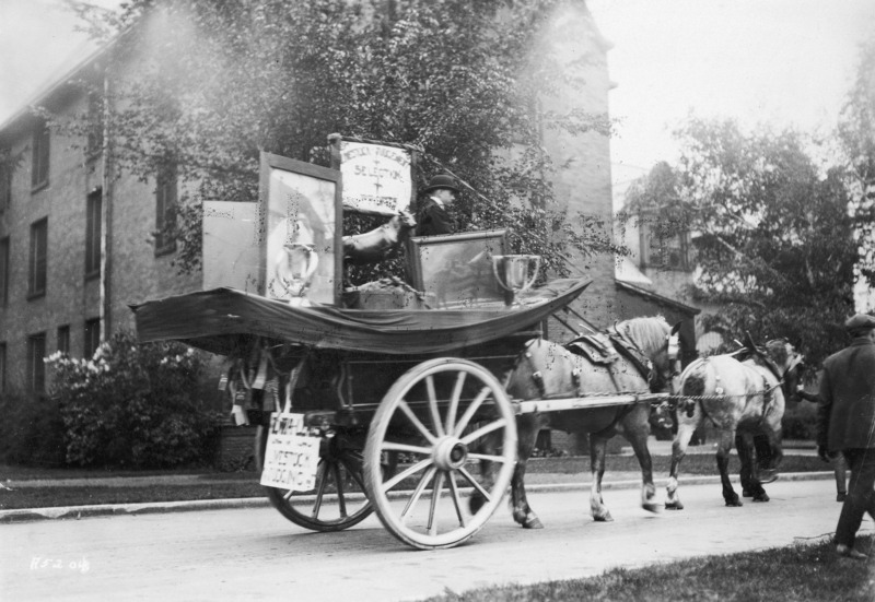 A 1923 horse-drawn VEISHEA Animal Husbandry float. The sign reads: "Livestock-Judgement Selection Profits." Margaret Hall can be seen in the background. See photograph 1722-2-3 for another view of the same float. "FILEPRINT NOT TO BE REMOVED FROM THIS FILE" has been stamped in ink.