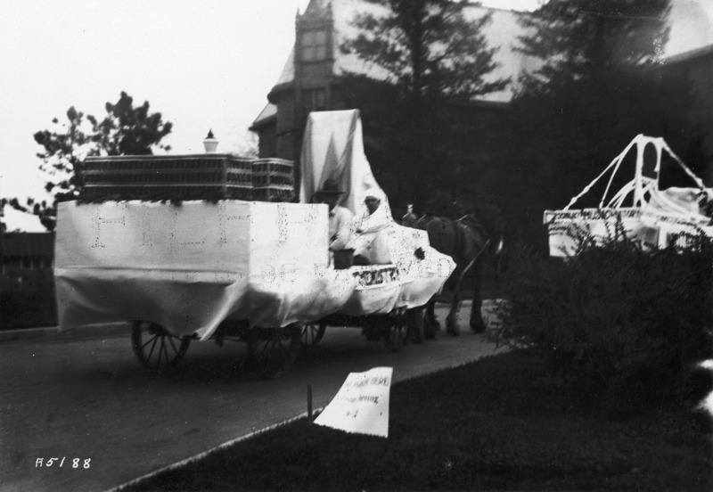 A 1923 VEISHEA Chemistry float. The horse-drawn float is mounted on a flat bed wagon. Viewed from behind, Margaret Hall can be seen in the background. See photographs 1722-3-2 and 1722-3-4 for other views of the same float.