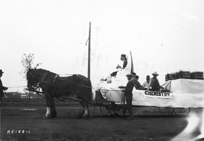 A 1923 VEISHEA Chemistry float. The horse-drawn float is mounted on a flat bed wagon. Viewed from behind, Margaret Hall can be seen in the background. See photographs 1722-3-2 and 1722-3-3 for other views of the same float.