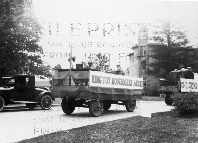 A banner with "King Tut Modernized AIEE" (American Institute of Electrical Engineers) is hung on the side of this float. There are three male students aboard, with various items including a fan and speaker.