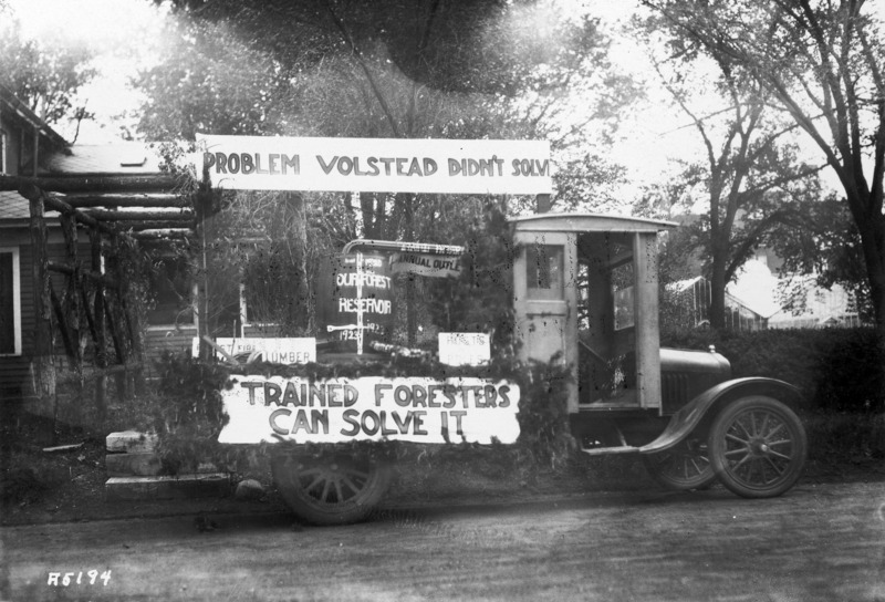 1923 float from the Forestry Department. "Problem Volstead Didnt Solve" on banner above. "Trained Foresters Can Solve It" on banner below. A barrel on the float says Our Forest Reservoir 1923.