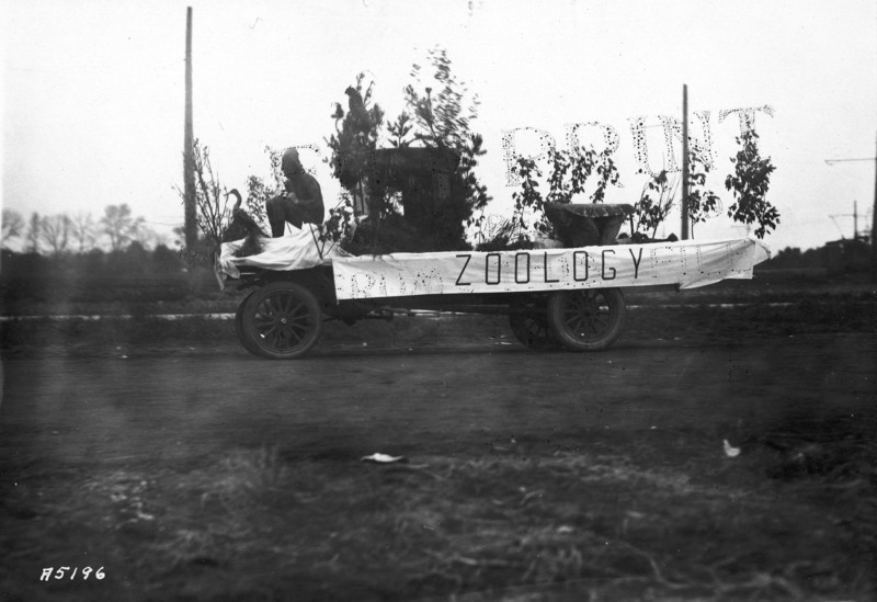 1923 motorized vehicle float from the Zoology Department. Depicts a wildlife scene with plants and animals (waterfowl and an owl) including two humans in costume.