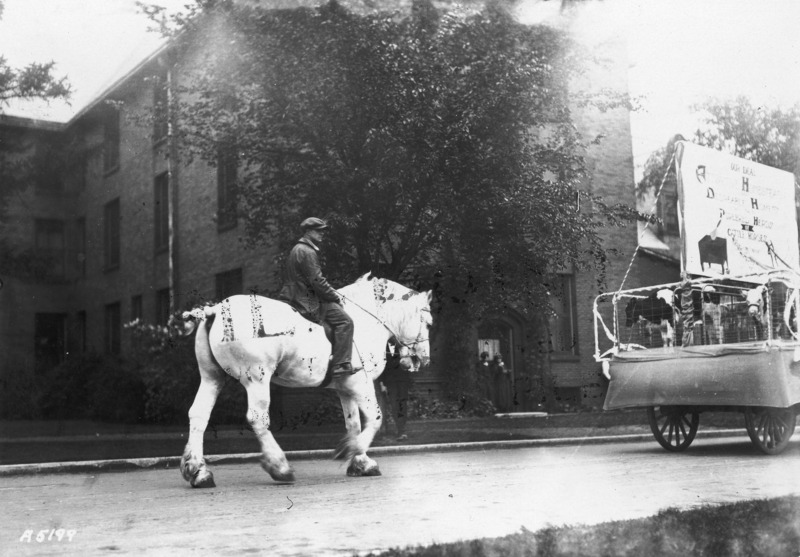 1923 horse-drawn float from the Department of Landscape Architecture. See photograph 1722-5-3 for alternate view of the same float. Potted plants and trellised plants create a garden for two girls to sit inside.