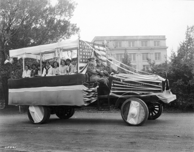 1923 motorized vehicle float with three member of ROTC in the front seat. Seated on the flat bed of the float are nine women, with another ROTC member behind them. See photograph 1722-5-8 for an alternate view.