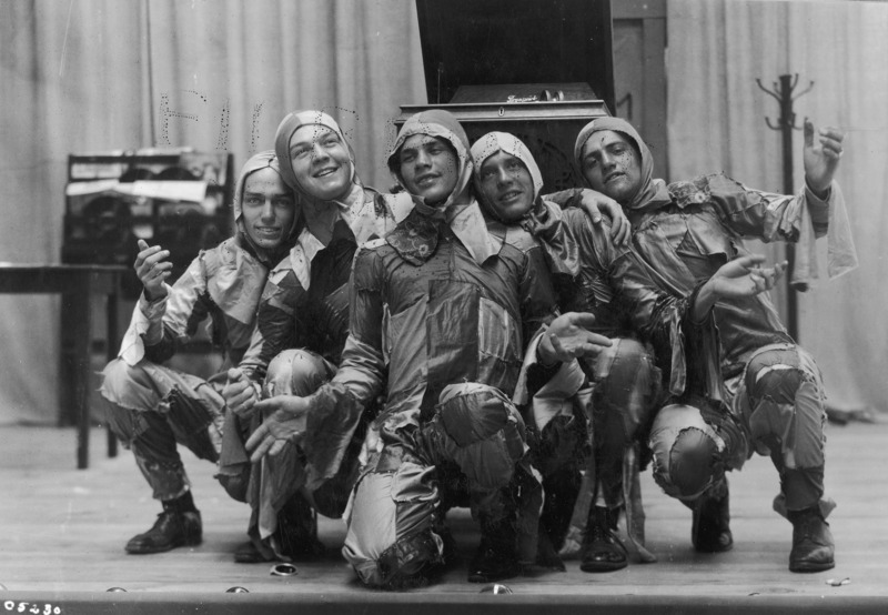 Five men in costume posing in kneeling positions in a scene from the VEISHEA Nite Show, "Melody Magic." The Nite Show is the predecessor to Stars Over VEISHEA. See photograph 1722-6-6 for another view of this scene.