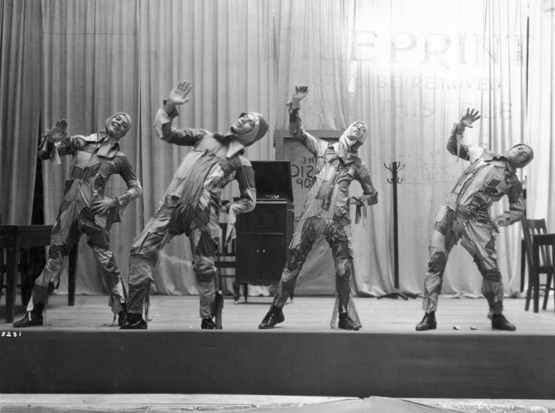 Four men in costume dancing in synchronicity in a scene from the VEISHEA Nite Show, "Melody Magic." The Nite Show is the predecessor to Stars Over VEISHEA. See photograph 1722-6-4 for another view of this scene.