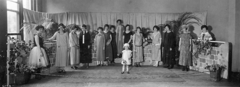 Photograph of the 1924 Home Economics Open House Display for clothing and textiles. The exhibit features women in various dresses and a little girl in a dress.