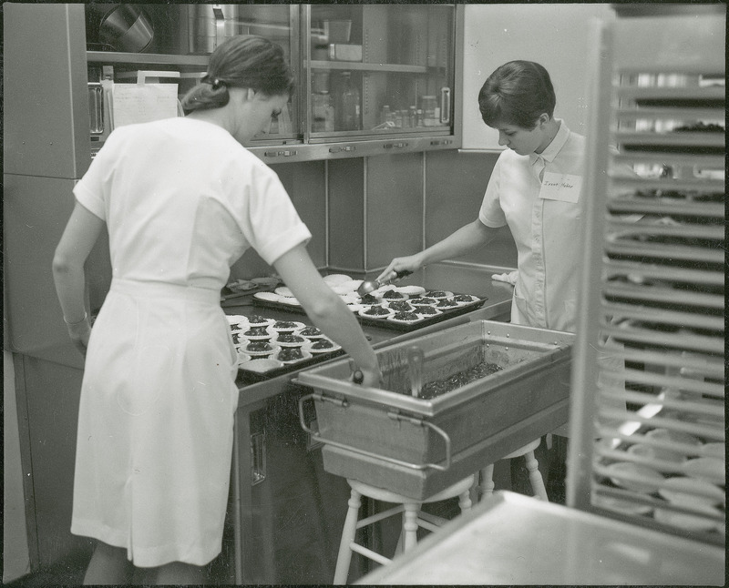 Making for the VEISHEA pies. A female students in the kitchen place cherry pie filling in the crusts.