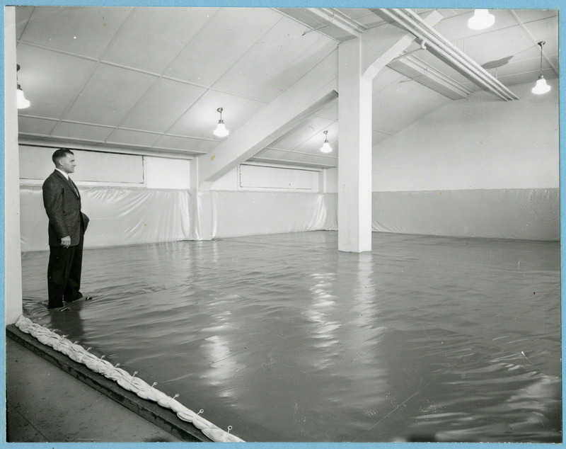 Wrestling coach Harold Nichols observes his wrestling room newly furnished with cardinal and gold mats, 1957.