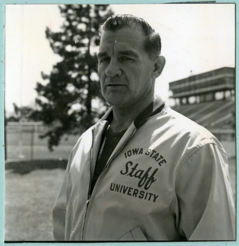 Wrestling coach Harold Nichols poses for a photograph. The stadium is in the background, 1965.