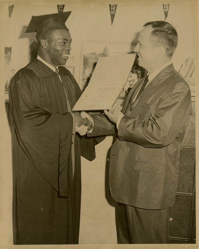 Football coach Clay Stapleton is shaking the hands of a graduate and presenting him with his diploma. Coach Stapleton was the head football coach from 1958-1967 and served as athletic director from 1967-1970, circa 1965.