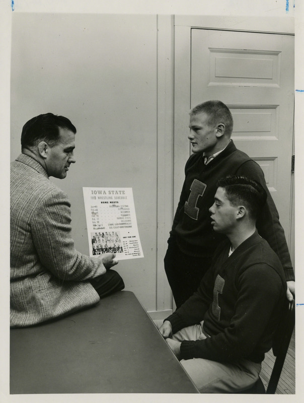 Wrestling Coach Harold Nichols shows wrestling schedule to Ron Gray (seated) and Les Anderson, both Iowa State University wrestlers, 1958.