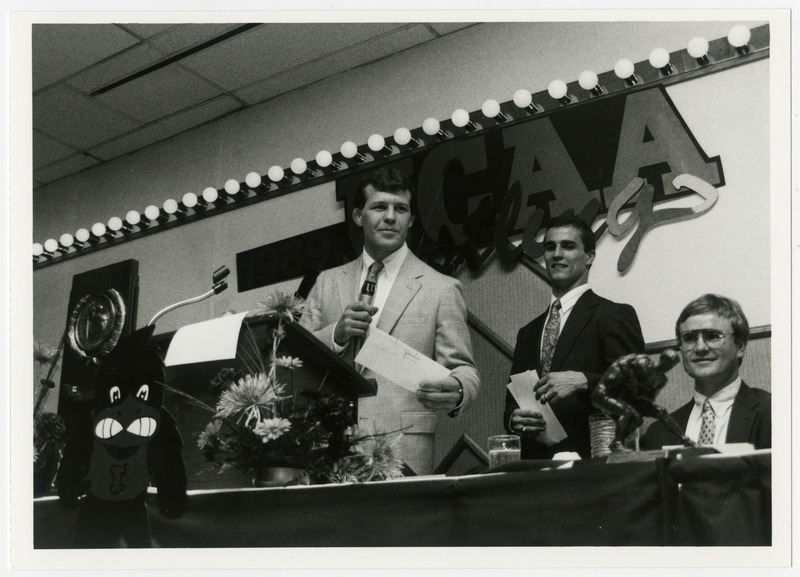 Three men standing behind a table, possibly at a wrestling awards ceremony, 1989.