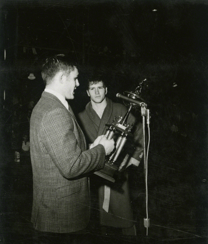 An unidentified man, holding a trophy, speaks to Dan Gable.