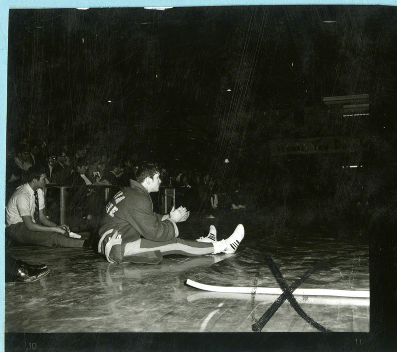 Dan Gable sits and claps, presumably at a wrestling event.