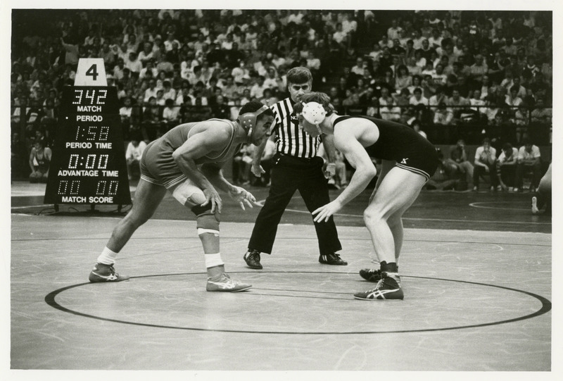 Two men are about to grapple. Referee stands in the background.