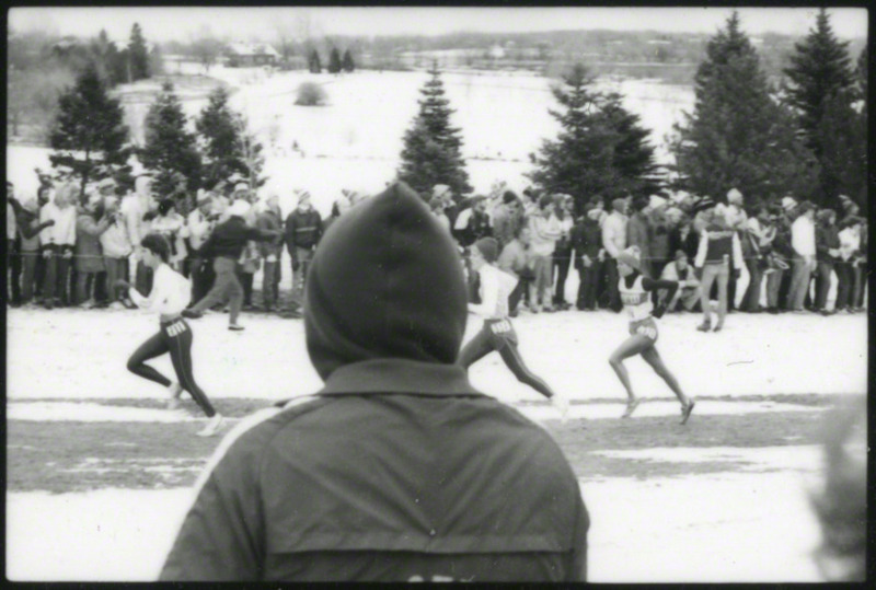 Several runners at the NCAA Women's cross-country meet Milwaukee, Wisconsin, on November 25, 1985, several hours before the plane crash. Spectator partially obstructs view.