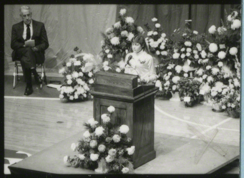 Bonnie Sons, cross-country runner, is at the podium giving a eulogy for coach Ron Renko.