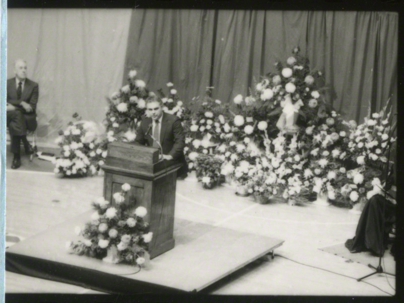 Max F. Urick, Director of Intercollegiate Athletics, is speaking from the podium at the memorial service, 1985.