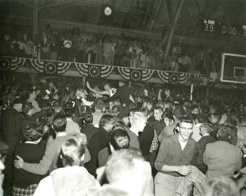 Fans and players on the court after the basketball game. Wilt Chamberlain (Kansas #13) stands in the crowd.