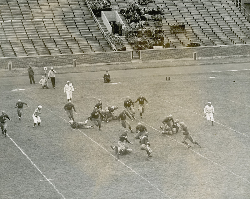 A football game between Iowa State University and Kansas State University. The photograph is taken from the stands. Small group of spectators watch from the stands in the background.