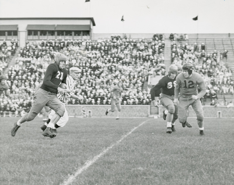 The close-up image shows a football game being played before a stadium of spectators. One player is identified as Meredith Warner.