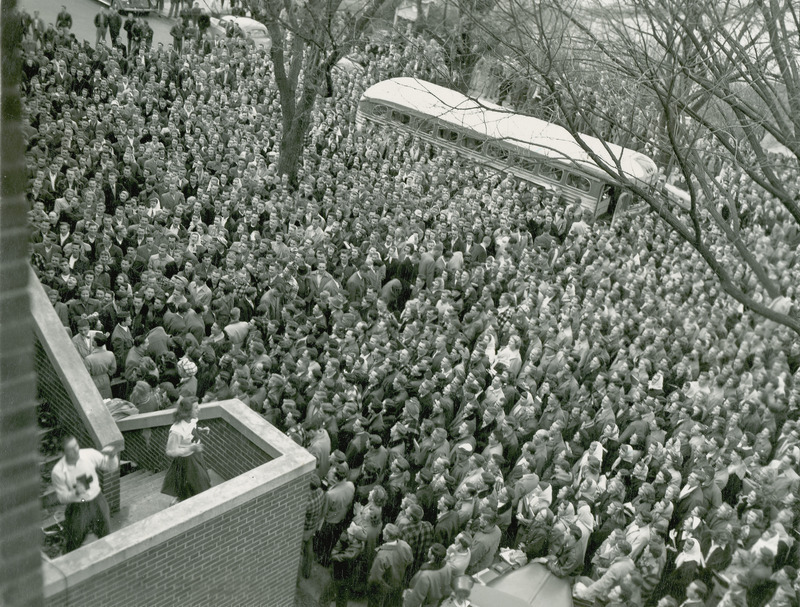 Pep rally before Arizona football game. A large group of individuals with busses and period cars in the background.