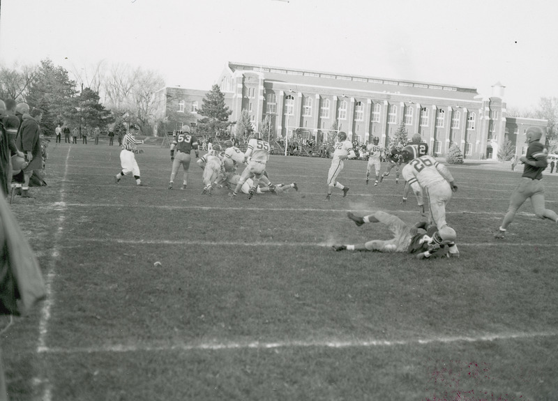 A football game in progress. State Gymnasium and the Marston Water Tower can be seen in the background. The back of the photograph notes this is the Iowa State College-Nebraska game.