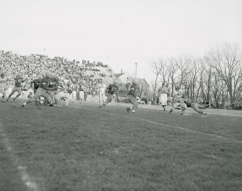 A football game in progress before a stand of spectators. The photograph caption identifies this as the Iowa State College versus Nebraska game.