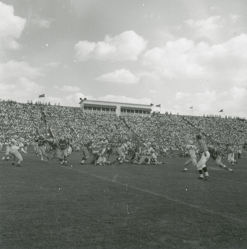 A homecoming football game being played before a stadium full of spectators. This image is part of a set of images that includes: 24-6-G.Football.1871-5-7-1; 24-6-G.Football.1871-5-7-3 ; and 24-6-G.Football.1871-5-7-4.