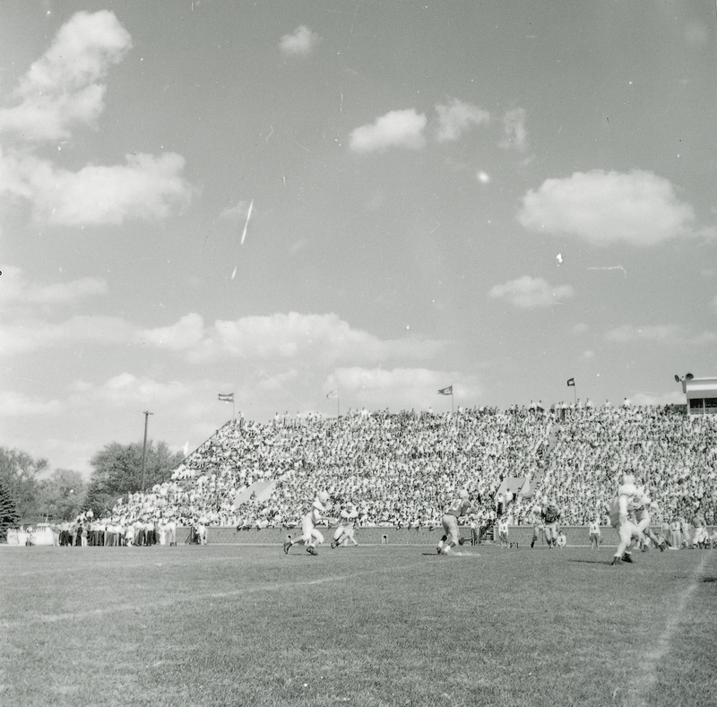 A homecoming football game being played before a group of spectators seated in a group of bleachers. This image is part of a set of images that includes: 24-6-G.Football.1871-5-7-1; 24-6-G.Football.1871-5-7-2 ; and 24-6-G.Football.1871-5-7-3.