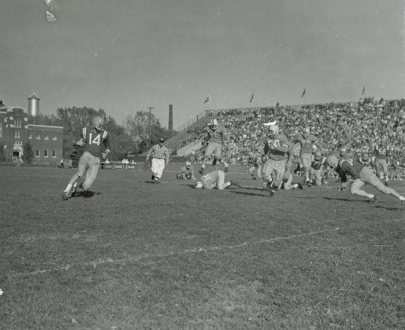 The ISC versus Drake football game in progress. In the background there are bleachers with spectators.