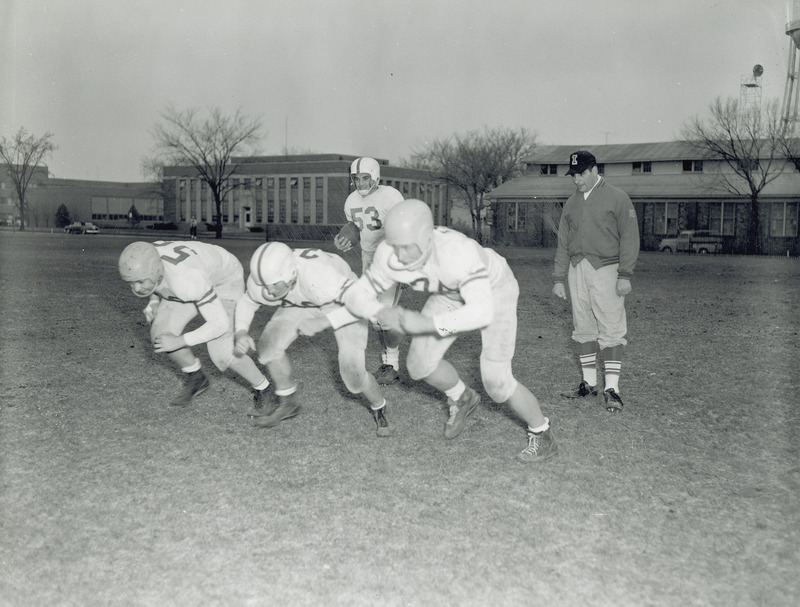 Coach Vince DiFrancesca, and football players Fred Rippel, Oliver Sparks, Ray Tweeten and Marv Walter in a posed action shot.