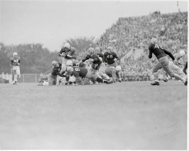 A football game in progress. A stadium full of spectators is in the background.