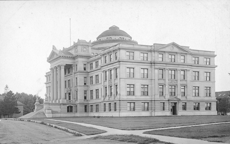 Beardshear Hall from a corner angle. No landscaping is present other than the grass lawn. The sidewalks shown are cement but the street is not paved.