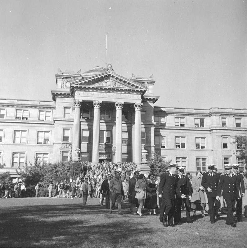 Beardshear Hall as the site for an event.A large number of people are on the steps, surrounding sidewalk, and on the walk leading across campus. Men in naval uniform (ROTC) are leading a procession away from Beardshear.