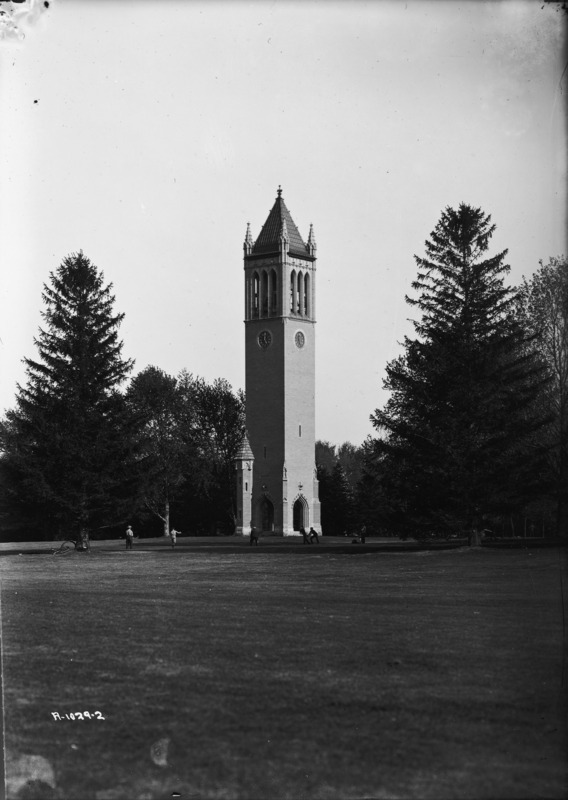 The Campanile in the summer of 1906. A small number of men are on the lawn in front of the Campanile, one of which appears to be throwing a ball. A bicycle is leaning against a tree on the left of the image.